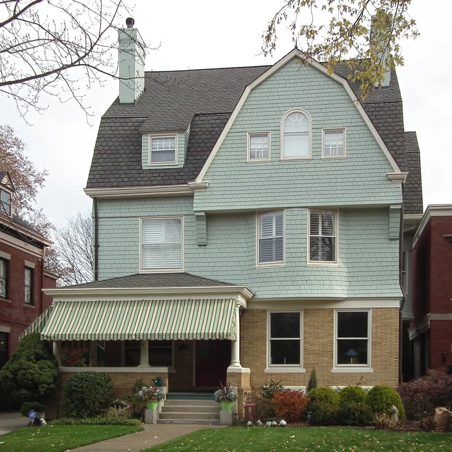 Pale green shingled two story home with a striped porch awning