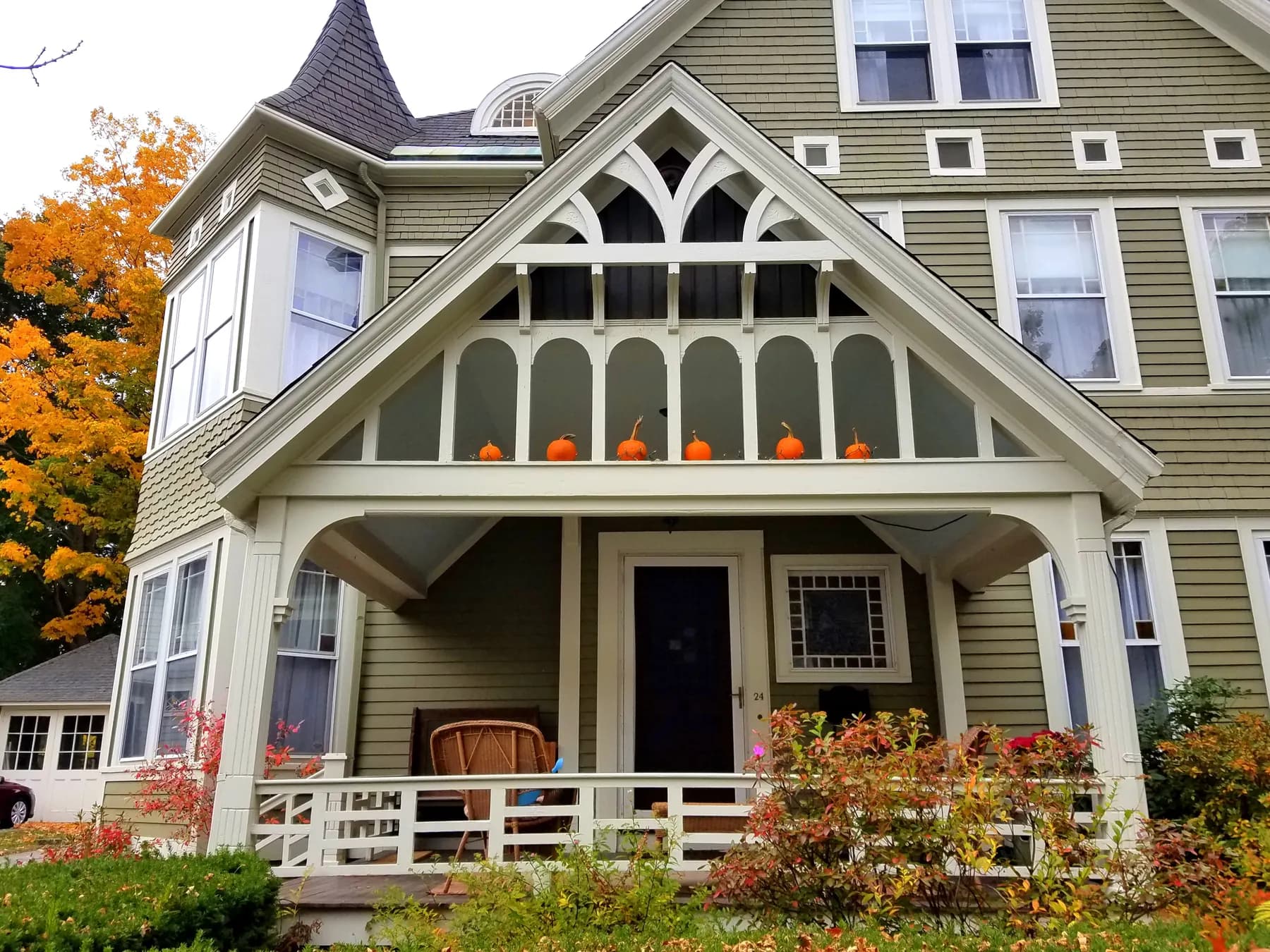Sage green Victorian home with a gabled porch and fall foliage