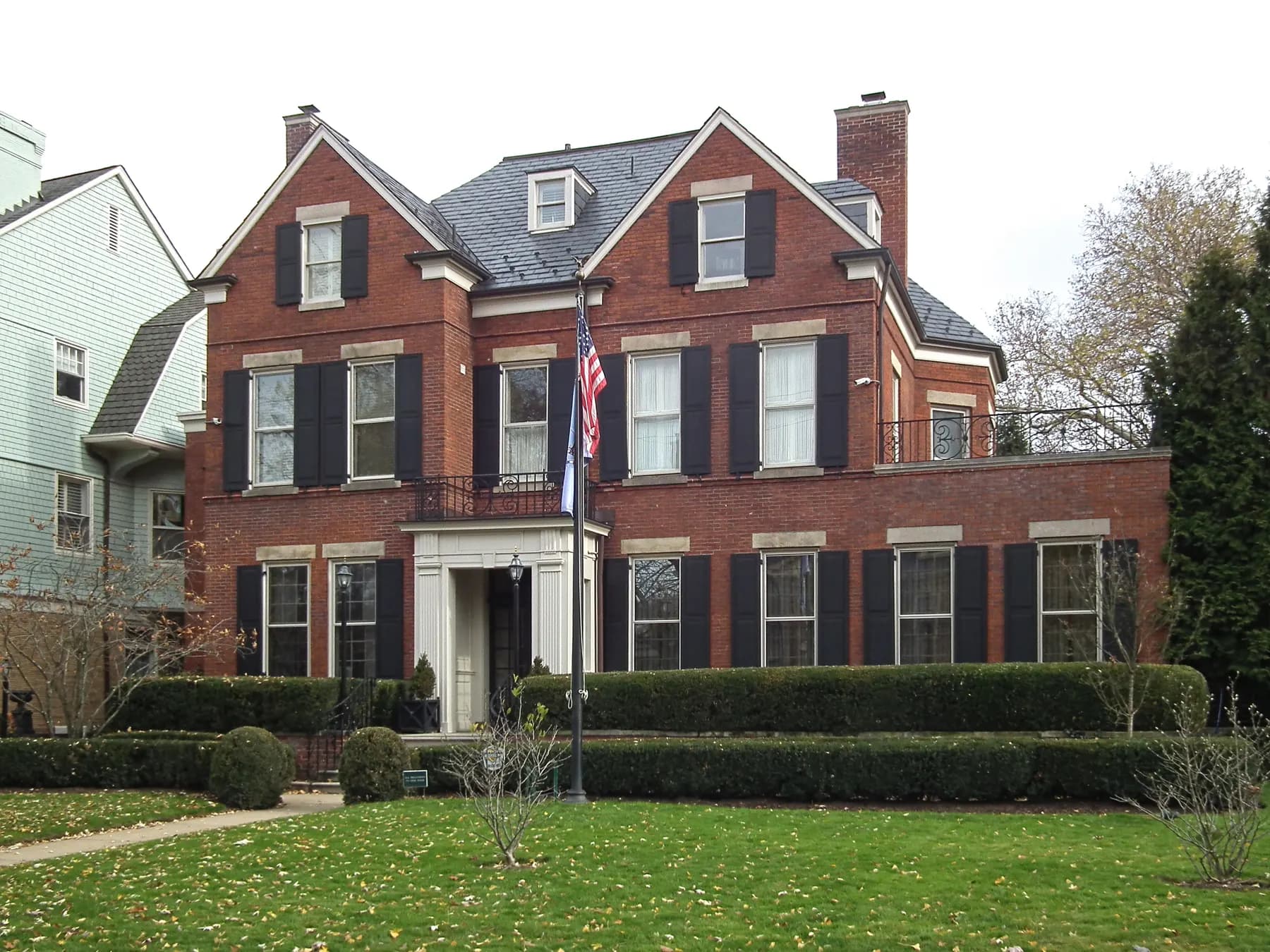 Red brick colonial home with black shutters and a clipped hedge