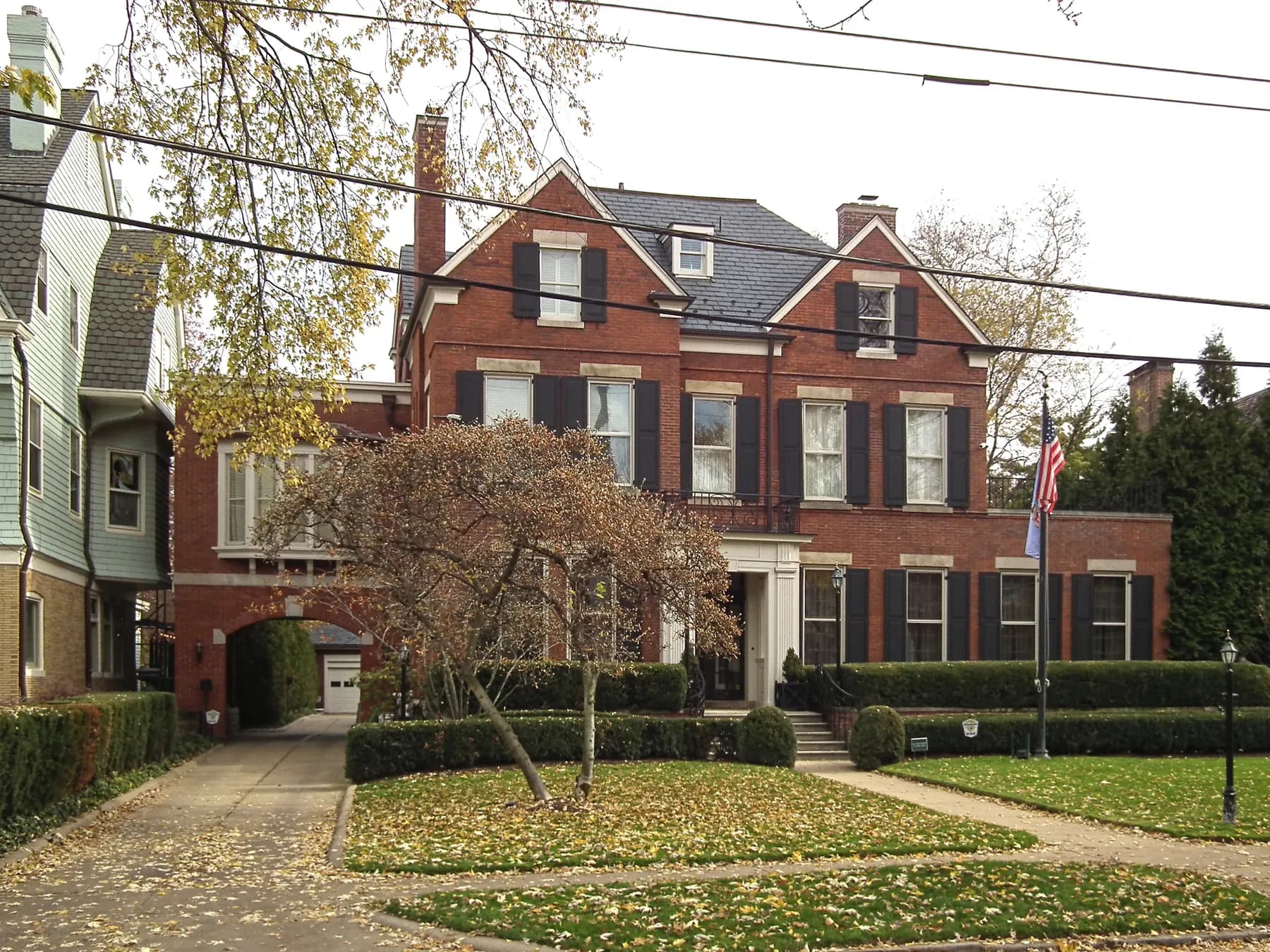 Red brick center hall home with black shutters and a fall lawn
