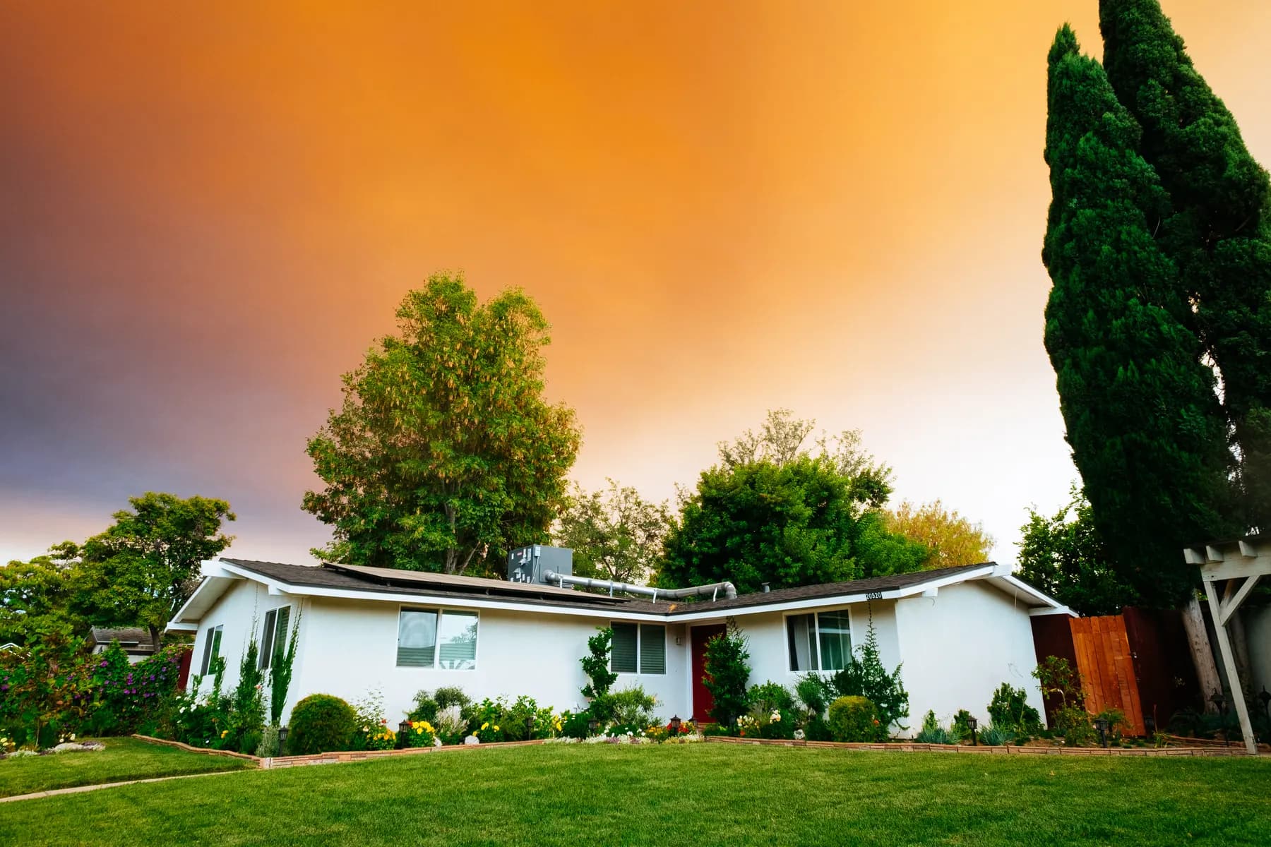Single story white ranch home with planting beds under a warm evening sky