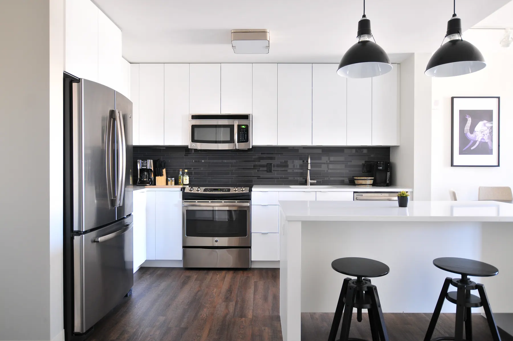 White kitchen with a quartz island, stools and pendant lights