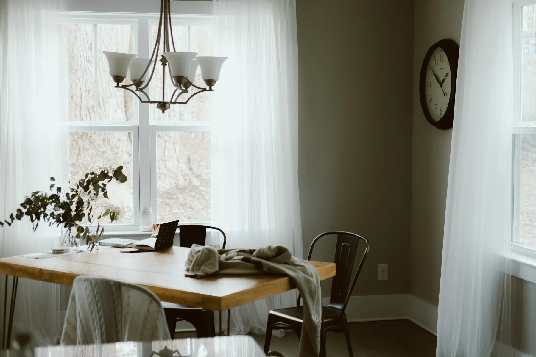 Breakfast nook with a wood table under a chandelier and sheer curtains